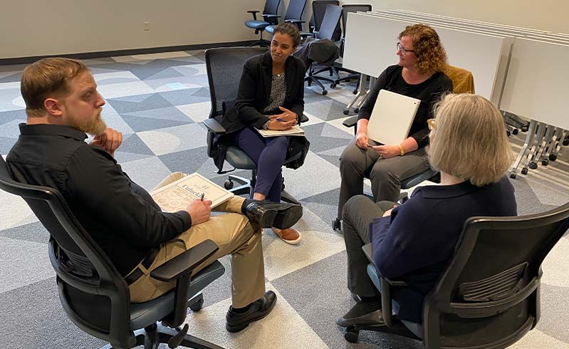Four women stand in a half-moon circle discussing leadership.